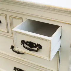 Biała komoda z ozdobnymi uchwytami, jedna szuflada lekko wysunięta. Inspiracje na odnawianie starych mebli.