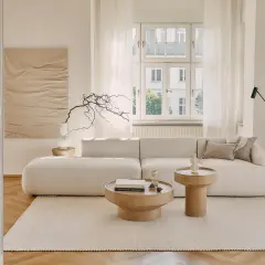 Jasny salon z sofą i stolikami kawowymi. Dominują odcienie beżu paleta kolorów, tworząc spokojną atmosferę.