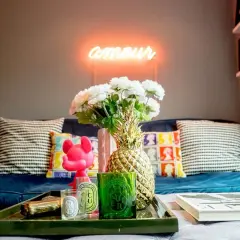 Jak ocieplić mieszkanie dodatkami: neon "amour", złoty ananas, świece i kwiaty na granatowej kanapie tworzą przytulną atmosferę.