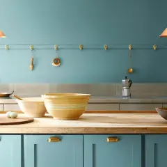 Niebieskie szafki kuchenne, drewniany blat, misy i jajka. Ściana pomalowana farbą ceramiczną w odcieniu błękitu.