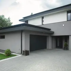 Nowoczesny dom z dwupoziomową, szarą elewacją, garażem i podjazdem z kostki brukowej.
