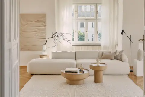 Jasny salon z sofą i stolikami kawowymi. Dominują odcienie beżu paleta kolorów, tworząc spokojną atmosferę.