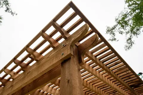 Drewniana pergola z ozdobnymi elementami. Dowiedz się, jak suszyć drewno, żeby nie pękało, by cieszyć się trwałą konstrukcją.