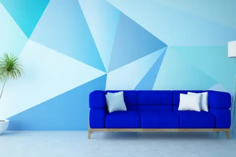 Niebieska sofa i geometryczne malowanie ścian – świetne malowanie ścian inspiracje. Roślina w donicy i lampa dopełniają nowoczesny wystrój.