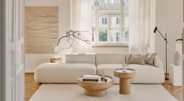 Jasny salon z sofą i stolikami kawowymi. Dominują odcienie beżu paleta kolorów, tworząc spokojną atmosferę.