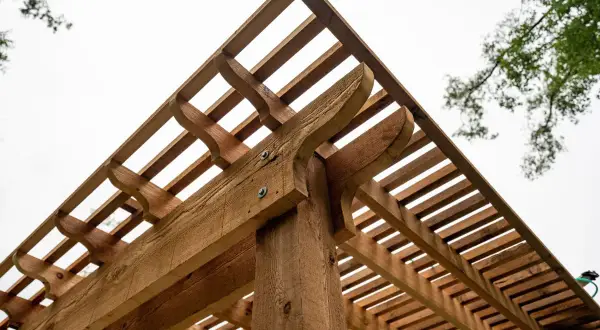 Drewniana pergola z ozdobnymi elementami. Dowiedz się, jak suszyć drewno, żeby nie pękało, by cieszyć się trwałą konstrukcją.