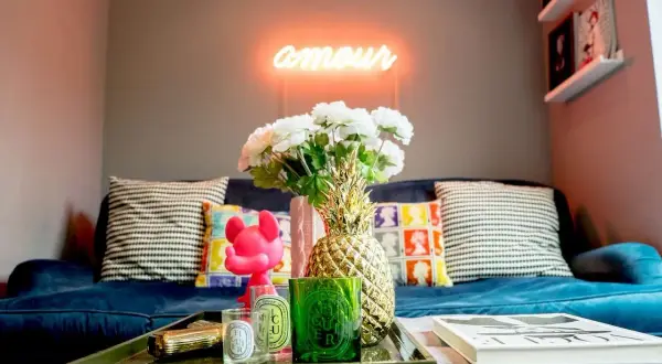 Jak ocieplić mieszkanie dodatkami: neon "amour", złoty ananas, świece i kwiaty na granatowej kanapie tworzą przytulną atmosferę.