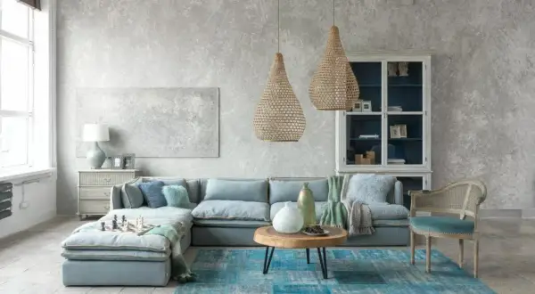 Nowoczesny styl prowansalski w salonie: błękitna sofa, plecione lampy, drewniany stolik i kamienna podłoga tworzą przytulną atmosferę.