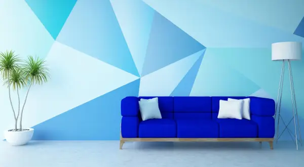 Niebieska sofa i geometryczne malowanie ścian – świetne malowanie ścian inspiracje. Roślina w donicy i lampa dopełniają nowoczesny wystrój.