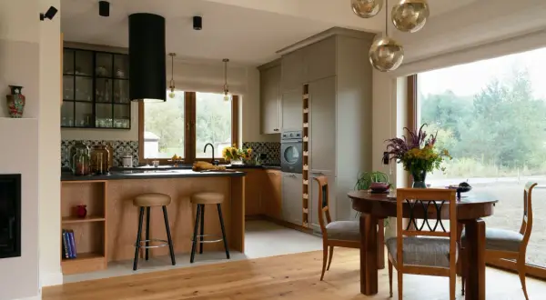 Nowoczesna kuchnia w stylu modern farmhouse z drewnianą wyspą, szarymi frontami i dużym oknem z widokiem na las.