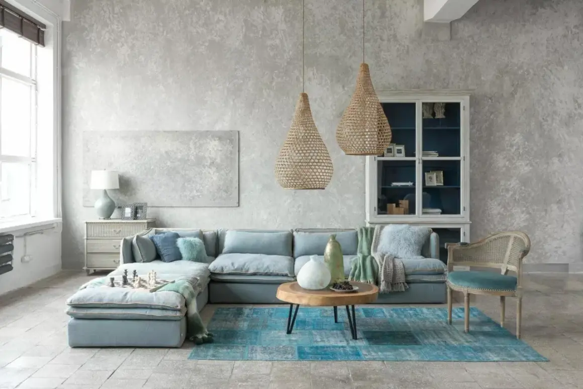 Nowoczesny styl prowansalski w salonie: błękitna sofa, plecione lampy, drewniany stolik i kamienna podłoga tworzą przytulną atmosferę.