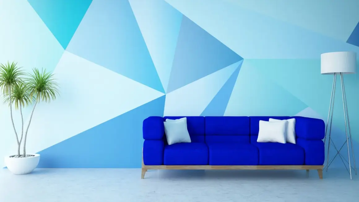 Niebieska sofa i geometryczne malowanie ścian – świetne malowanie ścian inspiracje. Roślina w donicy i lampa dopełniają nowoczesny wystrój.