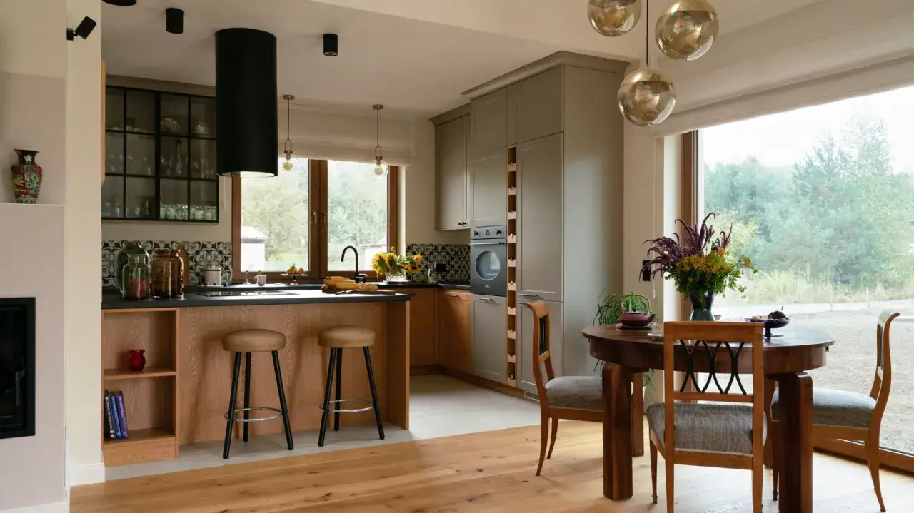 Nowoczesna kuchnia w stylu modern farmhouse z drewnianą wyspą, szarymi frontami i dużym oknem z widokiem na zieleń.