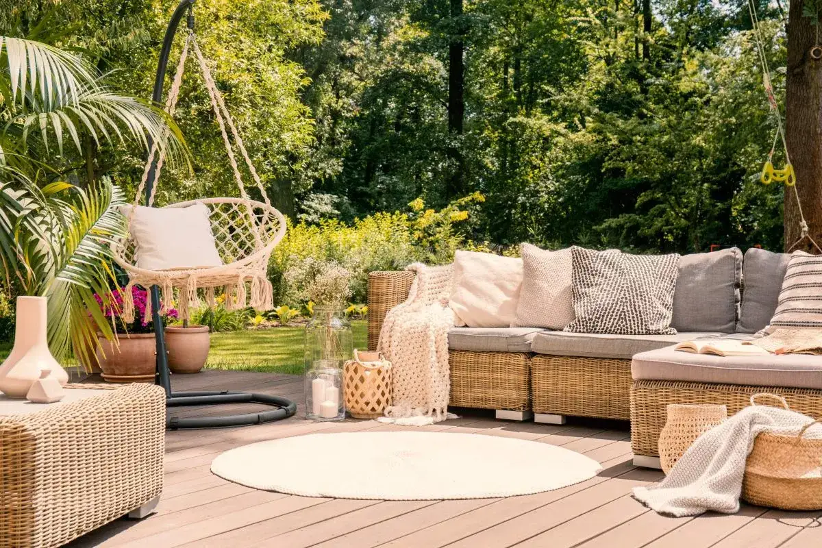 Relaks w ogrodzie w stylu boho: huśtawka z frędzlami, pleciona sofa z poduszkami, okrągły dywan i wiklinowe kosze tworzą przytulną atmosferę.