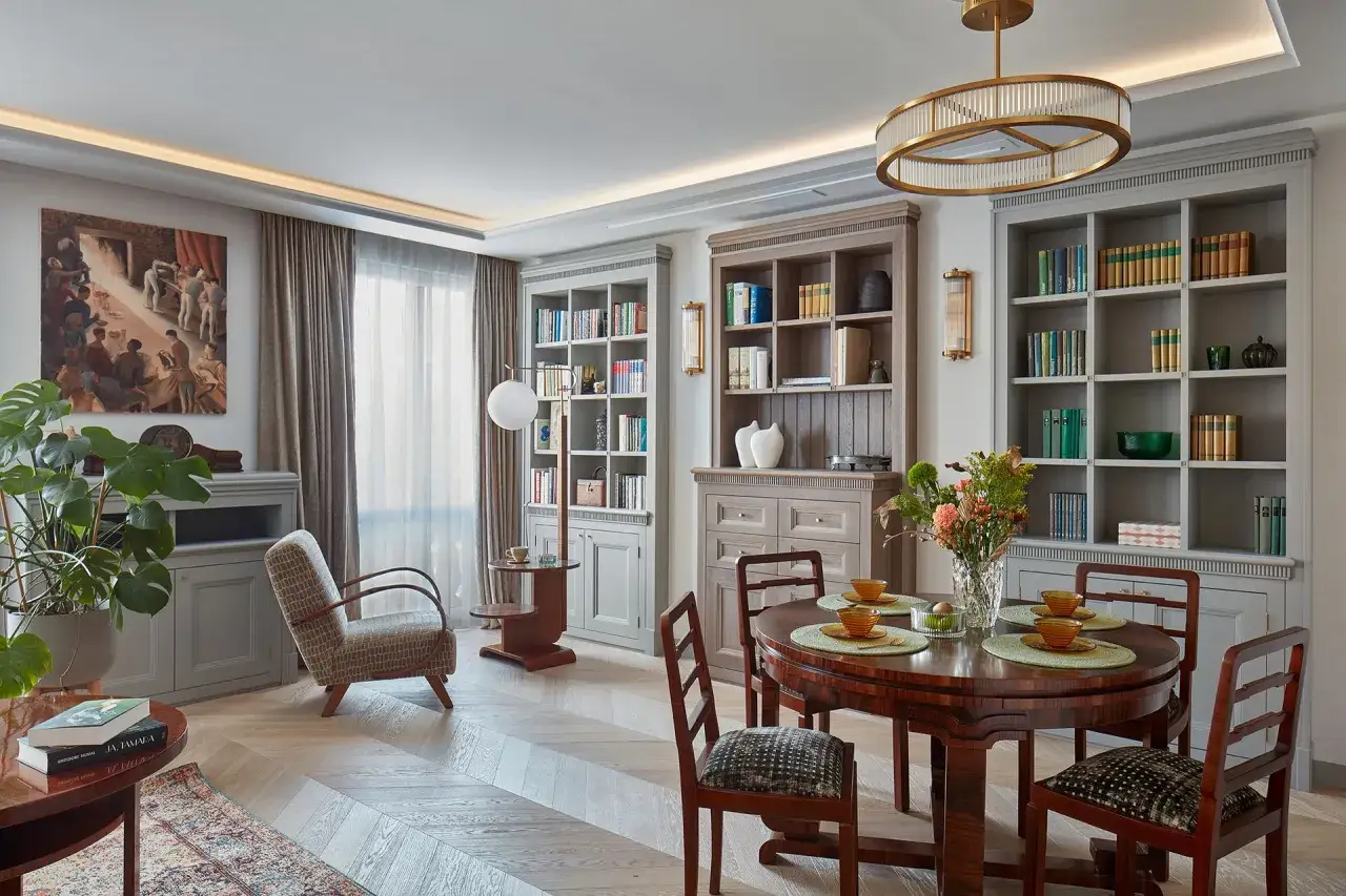 Eleganckie mieszkanie w kamienicy, inspiracje: salon z jadalnią, regały z książkami, okrągły st&oacute;ł, wygodny fotel i obraz na ścianie.