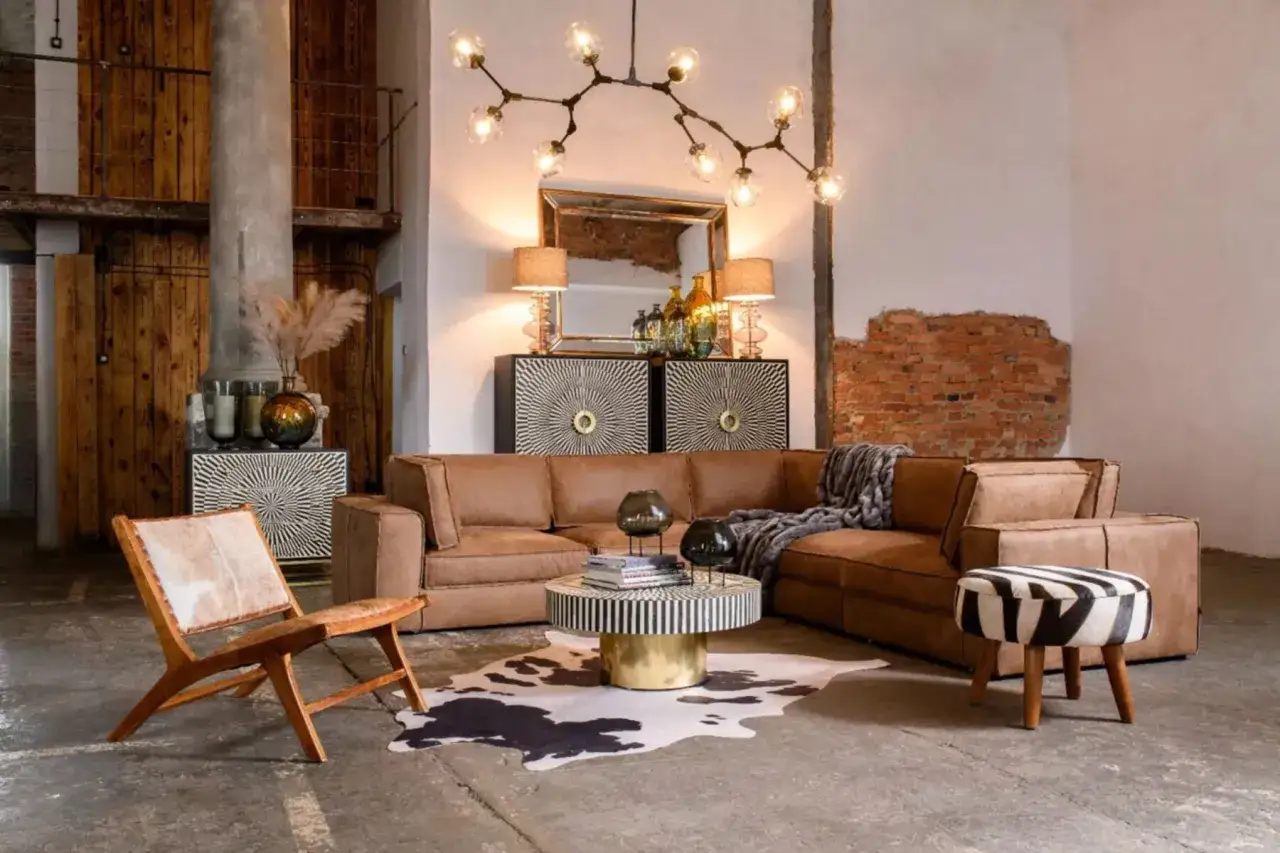 Stylowa aranżacja salonu w stylu loft: brązowa sk&oacute;rzana kanapa, drewniane meble, ceglana ściana i oryginalna lampa.