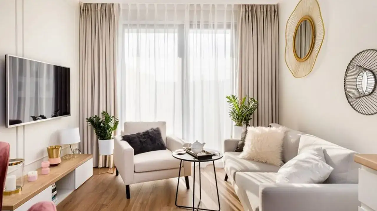 Mały salon aranżacje nowoczesne: jasna sofa, fotel, stolik kawowy, TV, rośliny i dekoracyjne lustra tworzą przytulną przestrzeń.
