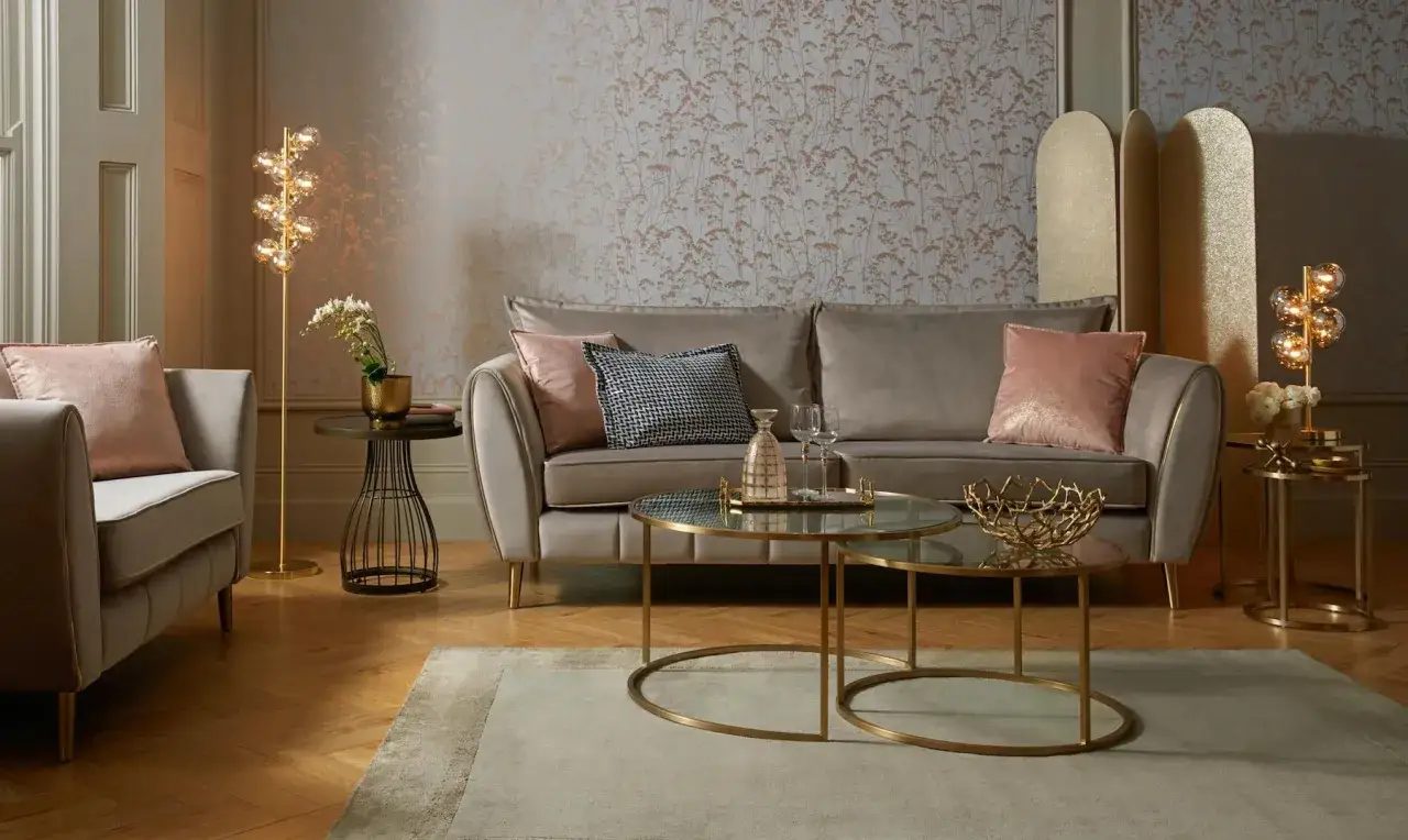Przytulny salon glamour z szarą sofą, r&oacute;żowymi poduszkami i złotymi akcentami.