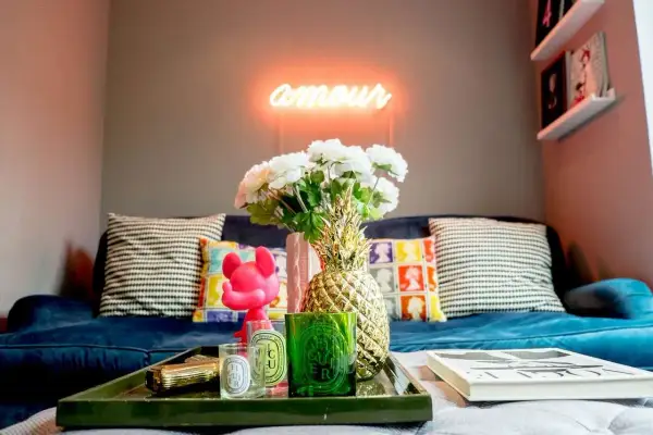 Jak ocieplić mieszkanie dodatkami: neon "amour", złoty ananas, świece i kwiaty na granatowej kanapie tworzą przytulną atmosferę.