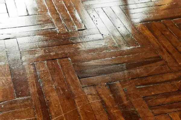 Wytarty lakier na parkiecie, widoczne ślady użytkowania i zmatowienia na drewnianej podłodze.
