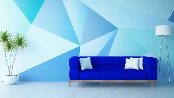 Niebieska sofa i geometryczne malowanie ścian – świetne malowanie ścian inspiracje. Roślina w donicy i lampa dopełniają nowoczesny wystrój.